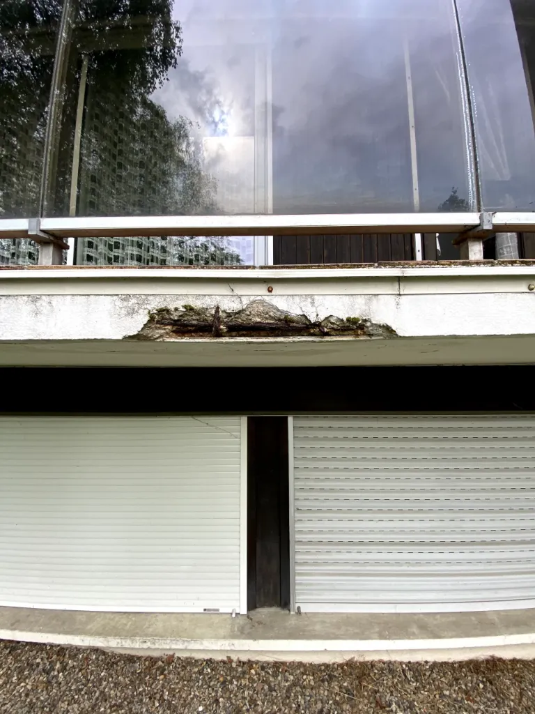 Vue d'ensemble du rebord de balcon montrant une armature en acier corrodée avec éclatement du béton, volets roulants en partie basse – diagnostic SODIAGS.