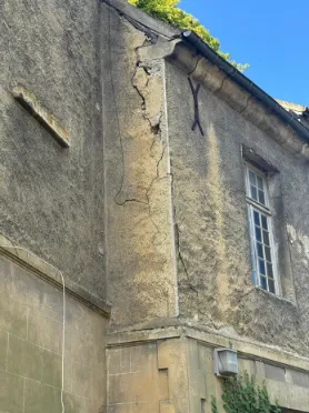 Fissure verticale importante visible sur un pignon de bâtiment avec ouverture apparente affectant la maçonnerie.